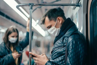 Korumalı maskeli yolcular metro vagonunda duruyorlar..