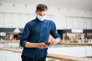 Sokakta duran akıllı telefonlu koruyucu maskeli bir adam.