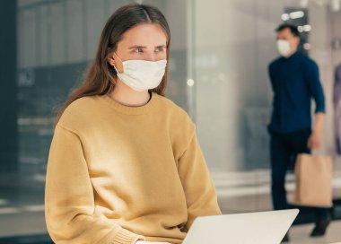 Dizüstü bilgisayar kullanan koruyucu maskeli genç bir kadın.