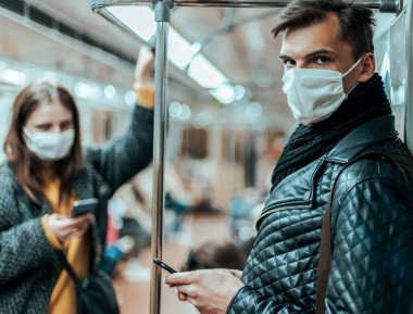 Korumalı maskeli yolcular metro vagonunda duruyorlar..
