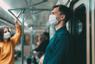 Koruyucu maskeli genç adam akıllı telefonunun ekranına bakıyor.