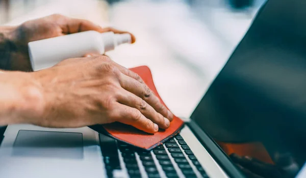 På nära håll. man sprutning spray på ytan av en bärbar dator — Stockfoto