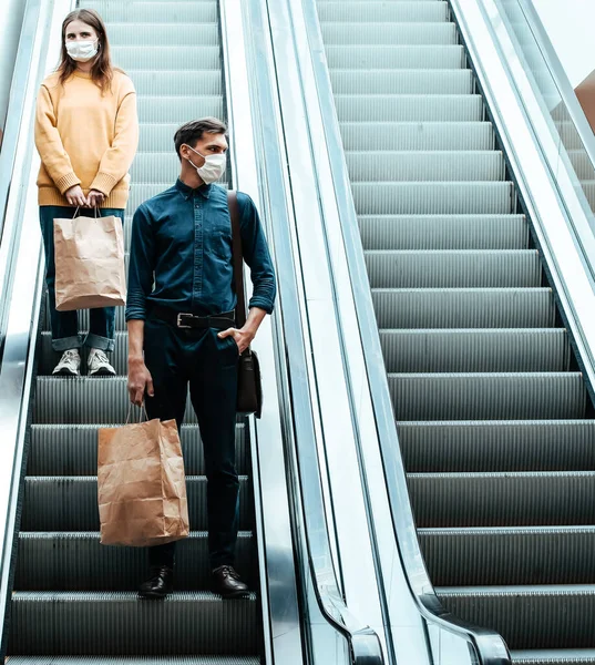 Junger Mann mit Schutzmaske steht auf einer Rolltreppe in einem Einkaufszentrum — Stockfoto
