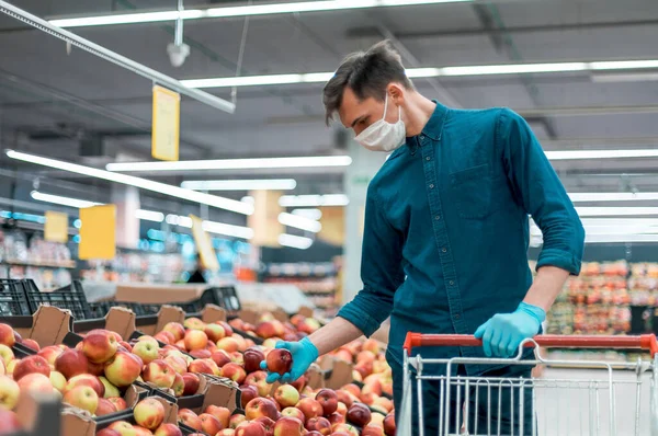 Jeune homme dans un masque de protection debout près du comptoir avec des pommes — Photo