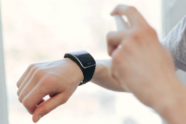 Genç adam akıllı saatine alkol antiseptiği püskürtüyor..