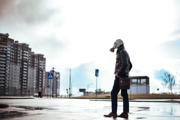 Casual jongeman in een gasmasker staan op straat in een geïnfecteerde stad. — Stockfoto