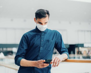 Sokakta duran akıllı telefonlu koruyucu maskeli bir adam.