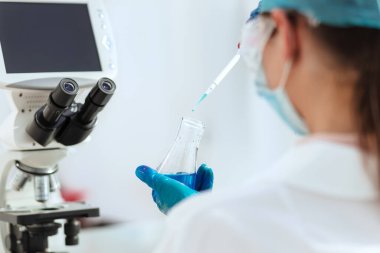 Kapat. Laboratuvar şişesinde sıvı test eden kadın laboratuvar asistanı..