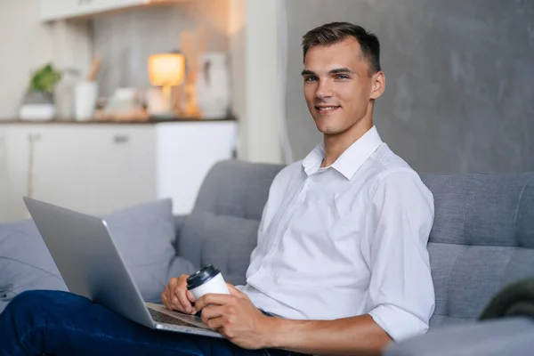 Mladý muž s laptopem sedící na pohovce v obývacím pokoji . — Stock fotografie