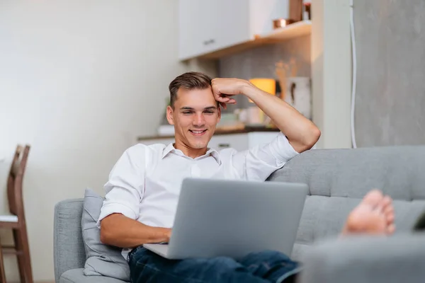Leende ung man bläddrar på Internet när du ligger på soffan. — Stockfoto