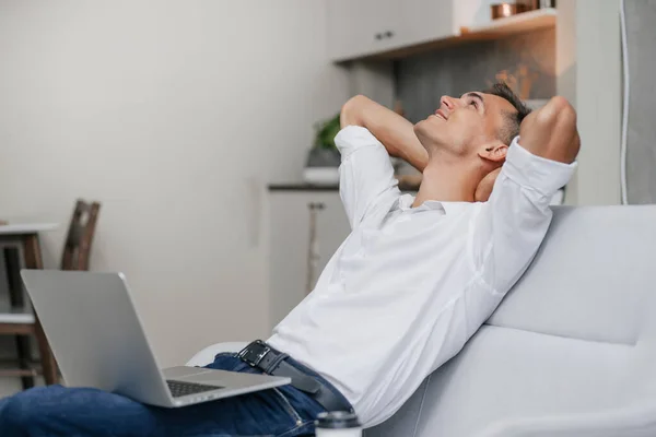 Drömmer ung man med en bärbar dator sitter på soffan. — Stockfoto