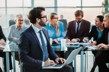 Ofis masasının önünde dizüstü bilgisayarlı bir iş adamı oturuyor.