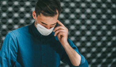 Kapat. Koruyucu maskeli çekici genç adam akıllı telefondan konuşuyor.