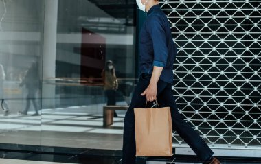 Koruyucu maskeli genç adam şehir caddesinde yürüyor.