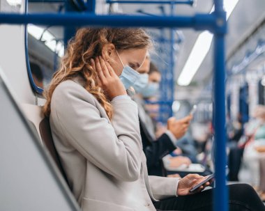 Koruyucu maskeli yolcular metro vagonunda aletlerini kullanıyorlar. .