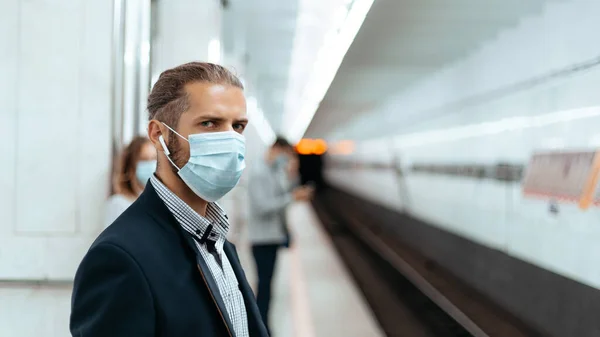 Jovem com uma máscara protetora em pé em uma estação de metro. — Fotografia de Stock