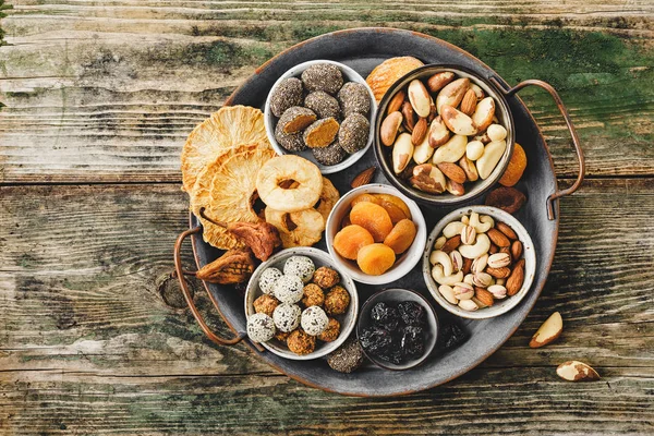 Mix of nuts and dried fruits on a old metal tray, rustic wooden table. Top view.