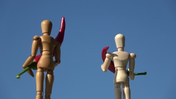 空を背景に2人の木製のアーティストマネキンを回転させ 赤唐辛子を保持する — ストック動画
