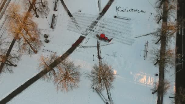市内公園広場から新鮮な雪を除去する小さな赤いトラクタークリーニング 空中ビュー — ストック動画