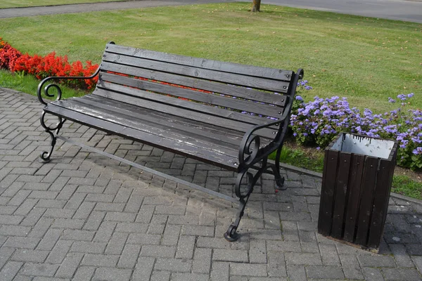 Modern wooden bench with metal frame in city street and flowerbeds — Stock Photo, Image