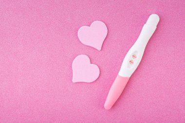 Pembe arka planda izole kalpler ile pozitif gebelik testi