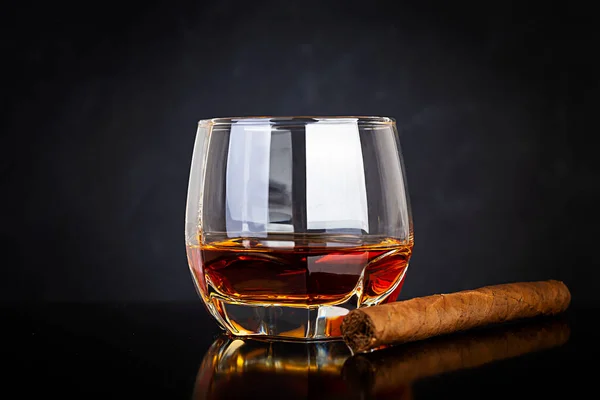 Glass of whiskey and cigar on dark background.