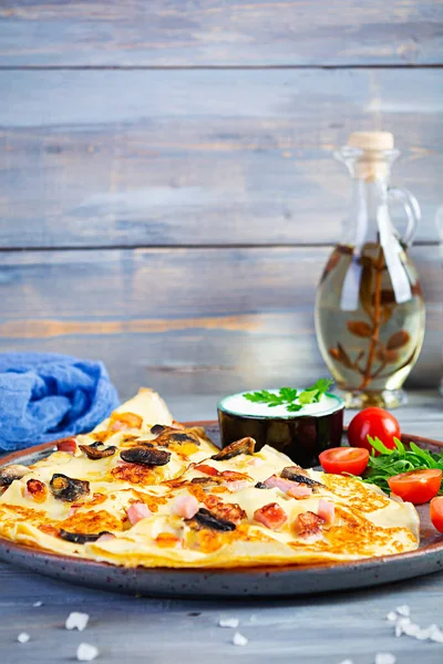 Delicious pancakes with mushrooms, ham and cheese, arugula, tomatoes and sour cream on a wooden background