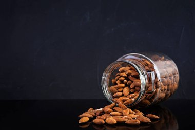 Kavanozda badem fıstığı. Karanlık arka planda izole edilmiş bir takım fındık