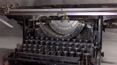 Usta eski daktiloyu yağlar. Bir video kamera monoton renkte bir masanın üzerindeki eski bir daktilonun yanından geçer..
