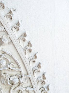 Tayland 'da bir tapınak duvarındaki beyaz bir duvar resmi. Geleneksel, karmaşık çiçek desenleri ve doğal ışık ve gölgelerle süslenmiş desenler sergiliyor..