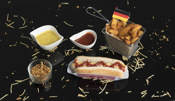 Hot dog s koření, omáčkami a bramborovými klíny v černém metha — Stock fotografie