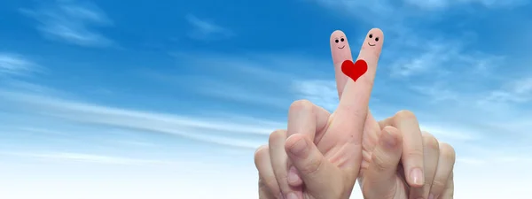 Concept or conceptual human or female hands with two fingers painted with a red heart and smiley faces over cloud blue sky background banner