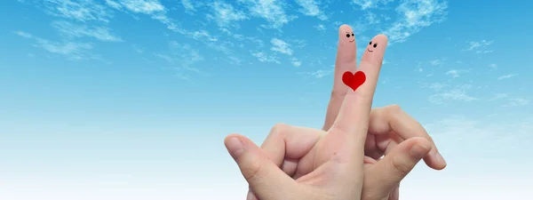 Concept or conceptual human or female hands with two fingers painted with a red heart and smiley faces over cloud blue sky background banner