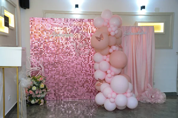 Pembe perde ve pullu fotoğraf arkaplanı. Ayrıca pembe ve beyaz balonların yanı sıra doğal çiçekli büyük bir buket vardır. Sırpça ve Kiril alfabesinde kadın adı Leonora ve Jovanoviç ailesinin soyadı