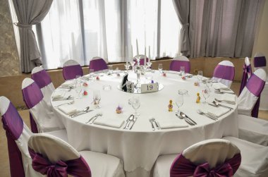 Düğün kutlamasında konuklar için bir yuvarlak masa. Mor detaylar 14 kişi için hazır.