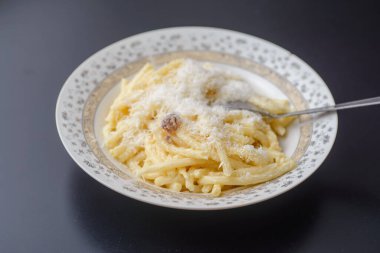 Beyaz bir tabakta siyah bir masada, içinde domuz pastırması, sarımsak, ekşi krema, yumurta ve dilimlenmiş parmesan peyniri bulunan Carbonara soslu spagetti. Lezzetli.