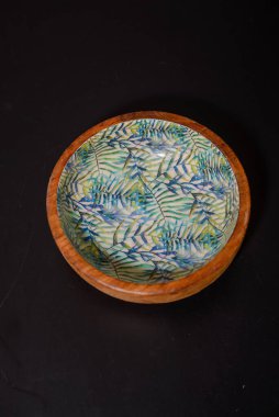 A round wooden bowl with hand-painted leaves on the inside that looks a bit like a jungle