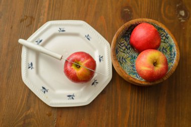 A knife that cut a red apple on a white plate