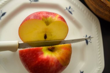 A knife that cut a red apple on a white plate