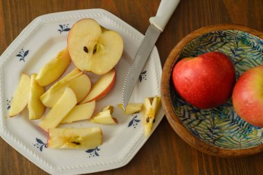 A knife that cut a red apple on a white plate