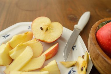 A knife that cut a red apple on a white plate