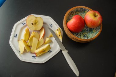 A knife that cut a red apple on a white plate