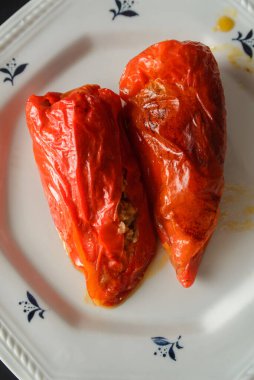 Doldurulmuş kırmızı dolma biber, içi et dolu, beyaz bir tabakta yemeye hazır.