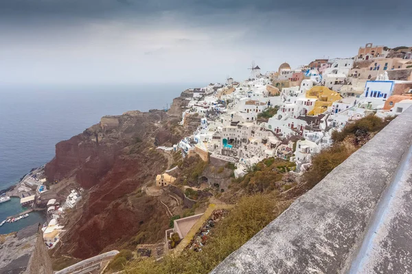 View of red cliffs and colorful houses of Oia on a rare rainy day — Stock Photo, Image