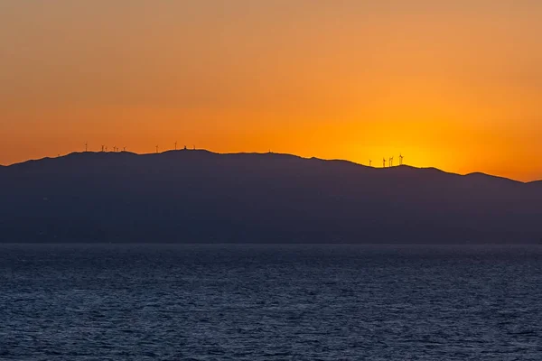 Сонце встановлює за профілем острова з вітровими турбінами — стокове фото