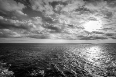 Güneşin kara ve beyaz etkisi denizin üzerindeki bulutların arasından süzülüyor.