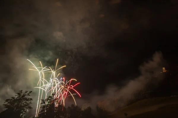 Geweldige witte en rode vuurwerk fonteinen boven bomen en een verlichte kerk — Stockfoto