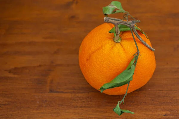 Orange with crumpled leaves on wooden blurred background