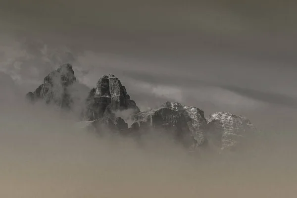 Schwarz-Weiß-Effekt der Dolomitengipfel, die in der Morgendämmerung aus niedrigen Wolken sprießen — Stockfoto