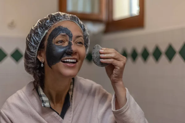 Close-up de uma mulher sorridente ao remover a máscara de lama de seu rosto — Fotografia de Stock